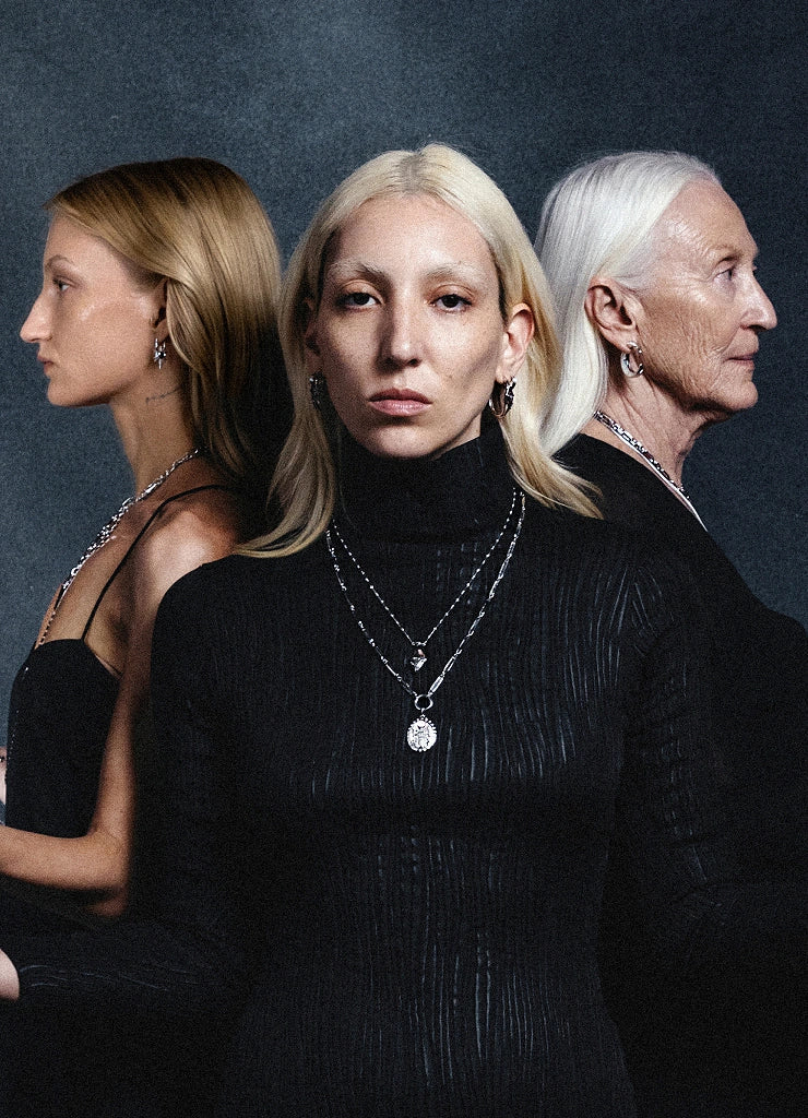 Product image of A person wearing layered silver necklaces and an earring. The necklaces feature a sun and moon pendant, a shell pendant, and another abstract pendant. The person is wearing a black shirt.