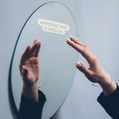 A woman's hand touching an Awe Inspired Affirmation Decal on a mirror.
