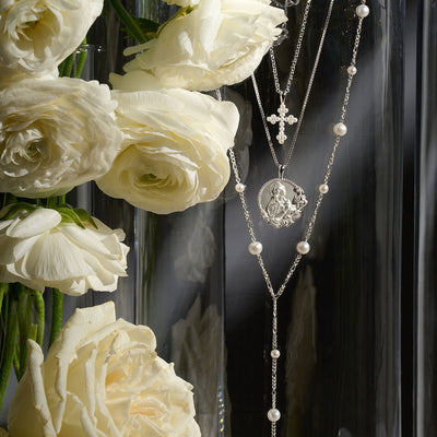 A vase with white roses and a Pearl Cross Amulet necklace from Awe Inspired.