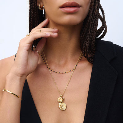 A woman wearing a black top and Awe Inspired Black Colored Enamel Necklace layered with mini Persephone pendant and standard Demeter pendant in gold vermeil.