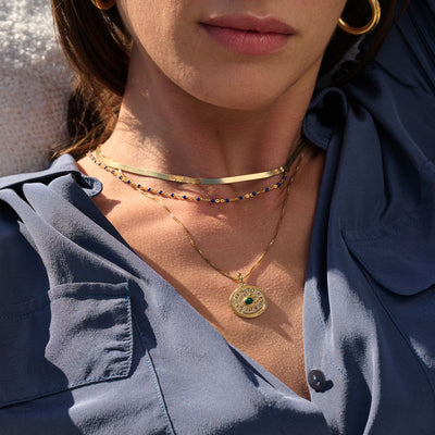 A woman is laying on the beach wearing a Say Yes to New Adventures Affirmation Coin Pendant necklace and earrings from Awe Inspired.