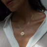 Close-up of a woman's neck and chest wearing the Awe Inspired Compass Locket Necklace over a white shirt. Her face is partially visible, and she has long dark hair.