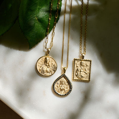 Three gold necklaces with a Gaia pendant from Awe Inspired on them.
