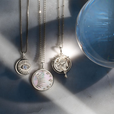 A collection of Celestial Mother of Pearl Amulet necklaces and an Awe Inspired crystal ball on a table.