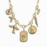 The Shattered Ceiling Statement Charm Necklace by Awe Inspired features a gold chain adorned with various charms, including a bird, a lion, a fist symbolizing Woman Power, and a "love" pendant.