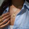 A person wearing a blue and white striped shirt showcases a gold necklace with an Awe Inspired Kamala Harris Pendant and multiple rings on their fingers.