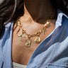 A person wearing a blue and white striped shirt showcases the Awe Inspired Shattered Ceiling Statement Charm Necklace, adorned with various empowering charms.