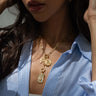 A person wearing a blue and white striped shirt is seen sporting the Awe Inspired Vote Pro-Roe Charm Lariat Necklace Set, adorned with three pendants—a coin, a symbol, and a Kamala Harris pendant from the 2024 Election Edition.