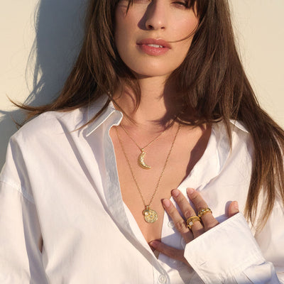 A woman wearing a white shirt and Awe Inspired's Moonstone Crescent Amulet necklace.