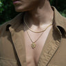 A person wearing a tan button-up shirt with gold necklaces, one featuring the Special Edition Medusa Necklace by Awe Inspired, believed to be a symbol of protection.