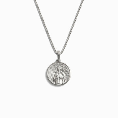 The Mini Aphrodite Necklace by Awe Inspired is a silver pendant necklace featuring a round medallion adorned with an intricate design inspired by Aphrodite, the Goddess of Love. The fine box link chain exudes sensuality in every detail.