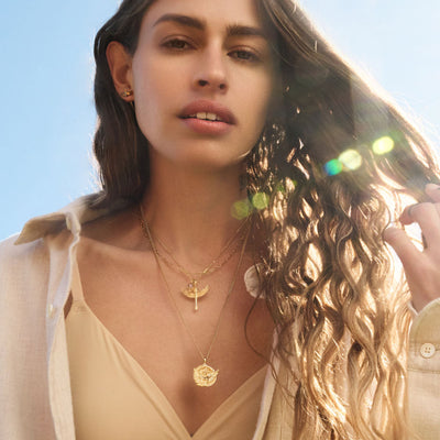 A woman wearing a white shirt and an Awe Inspired Winged Torch Amulet necklace.