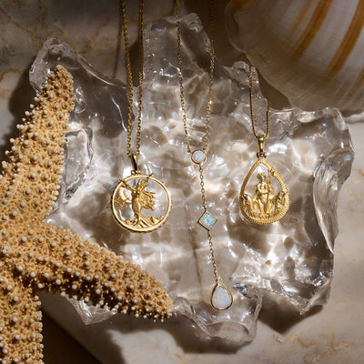 Necklaces laid on crystal featuring Yemaya pendant on the cable chain, opal drop necklace, and Amphitrite pendant on a box chain all in gold vermeil.