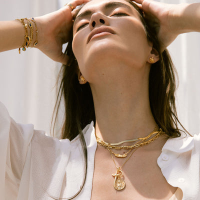 A woman wearing a white shirt and Awe Inspired's Divine Feminine Necklace layered with Flying Dagger amulet, standard Athena pendant and Herringbone chain in gold vermeil