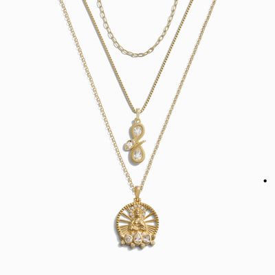 The Seek Enlightenment Necklace Set by Awe Inspired includes three gold necklaces featuring unique pendant designs: an Infinity Snake, a tree motif symbolizing spiritual enlightenment, and a round peacock medallion with hanging pearls.