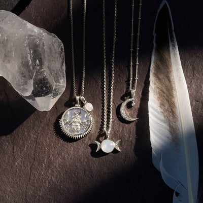 A collection of Triple Moon Amulets and crystals on a stone from Awe Inspired.