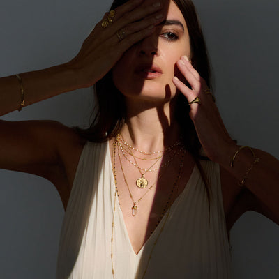 A woman wearing a white dress and Awe Inspired Crystal Quartz Amulet necklaces.