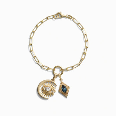 Awe Inspired's Invisible Aura Charm Bracelet: A gold chain bracelet adorned with two exquisite charms—a crescent moon featuring a Watchful Moon Eye and a central crystal, and a diamond-shaped charm with a dark central stone.