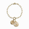 The Ocean Goddess Charm Bracelet by Awe Inspired features a gold-toned chain with two exquisite charms: a profile-engraved coin and a pearl-like seashell, exuding timeless beauty.