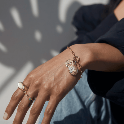 A close-up of a person's hand adorned with the Ocean Goddess Charm Bracelet from Awe Inspired and a ring featuring a large pearl. The person, dressed in a dark long-sleeve shirt, exudes beauty and elegance.