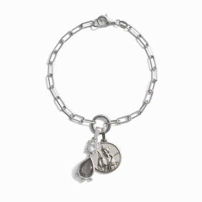 The Wild Goddess Charm Bracelet by Awe Inspired is a silver chain bracelet with a clasp, featuring three beautiful charms: a clear gemstone, a teardrop-shaped stone, and an engraved coin-like charm. This elegant piece channels the spirit of the Goddess of the wilds through its bezel-set gemstones.