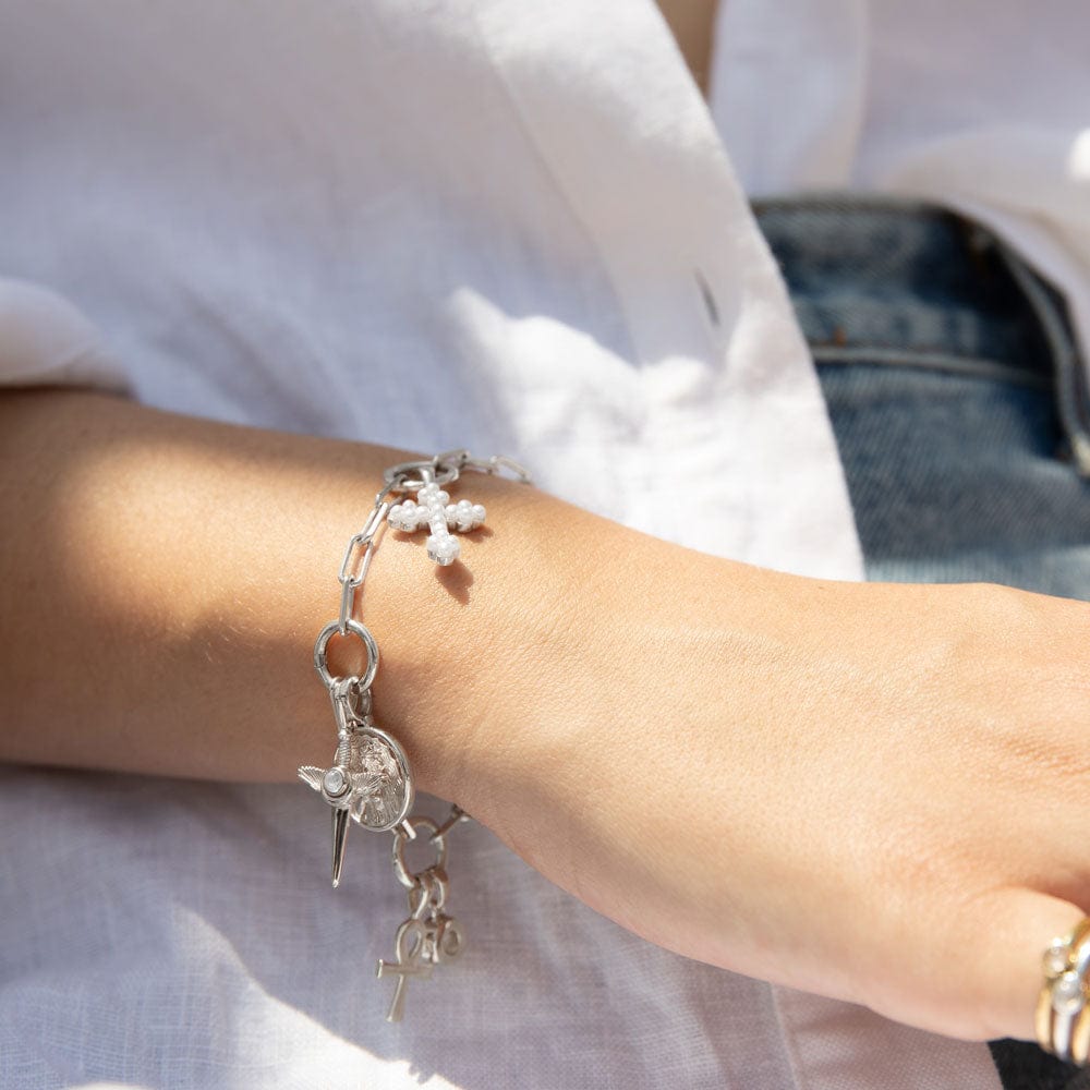 Close-up of a person wearing The Charm Collector Bracelet by Awe Inspired, adorned with a cross, heart, and various small charms, capturing the 90s charm bracelet aesthetic. The background reveals part of a white shirt and denim jeans.
