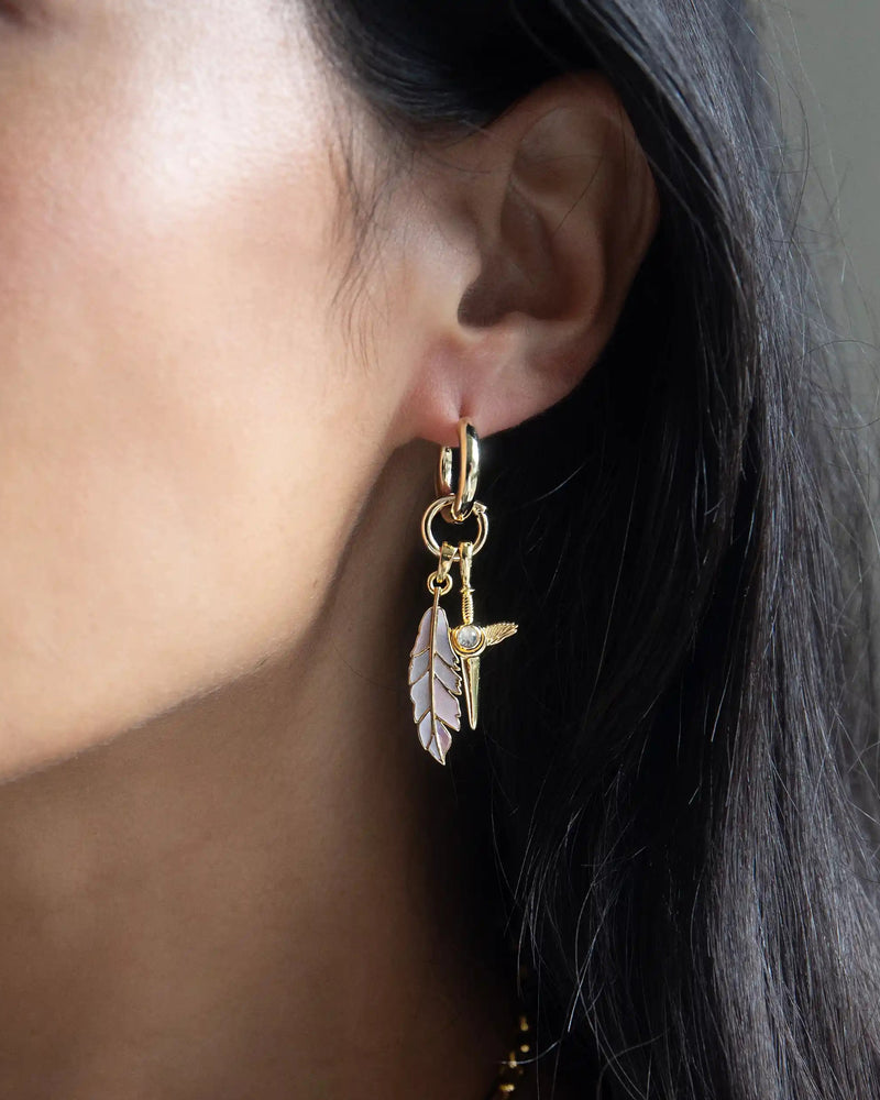Close-up of a person wearing the Mother of Pearl Feather Amulet by Awe Inspired, featuring a white feather and bird charm reminiscent of Athena's power.