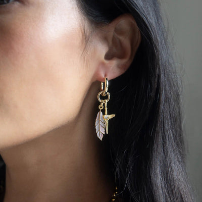 Close-up of a person wearing the Mother of Pearl Feather Amulet by Awe Inspired, featuring a white feather and bird charm reminiscent of Athena's power.