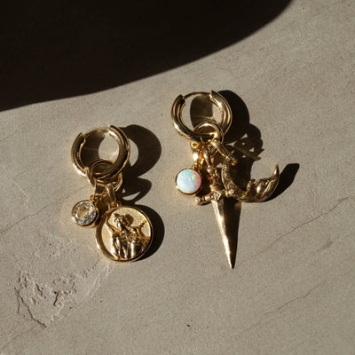 A pair of The Charm Collector Earrings by Awe Inspired rests elegantly on a concrete surface, perfect for any charm collector.