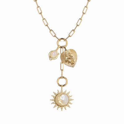 The Love Goddess Lariat Charm Necklace by Awe Inspired features a gold chain with heart, lion head, pearl drop, and celestial motifs, including a sun-shaped pendant with a pearl center.