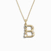 The Gold Gemstone Initial Necklace by Awe Inspired features a gold necklace adorned with a statement-sized initial charm in the shape of the letter "B," embellished with various small bezel-set gemstones.
