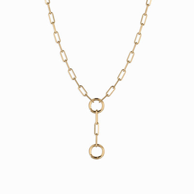 The Awe Inspired Lariat Charm Collector Necklace boasts a gold chain with rectangular links and a dangling vertical section adorned with two round loops, making it an ideal addition to any Awe charms collection.