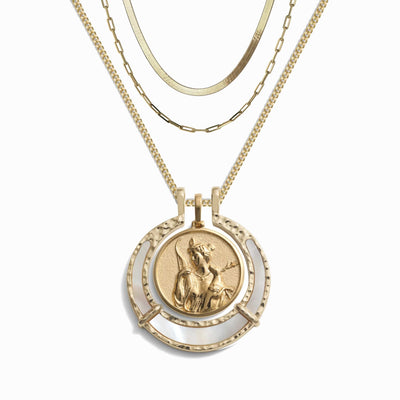 The Hunter's Moon Halo Necklace Set by Awe Inspired features a gold necklace with four layered chains, including one adorned with an Artemis pendant showcasing a raised image of a figure.