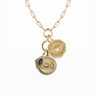 The Cosmic Affirmation Charm Necklace by Awe Inspired is a gold piece with three circular pendants featuring unique designs: one showcases a Cosmic Eye motif, another an octagon shape with the affirmation "ANYTHING CAN HAPPEN," and the third is adorned with a shimmering gemstone.