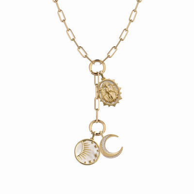 The Lilith Moon Charm Lariat by Awe Inspired features a gold chain with three dangling charms: a round sun charm, a crescent moon with star charm symbolizing the dark side of the moon, and an oval religious medallion. Set against a plain white background, this captivating piece is beautifully presided over by Lilith.