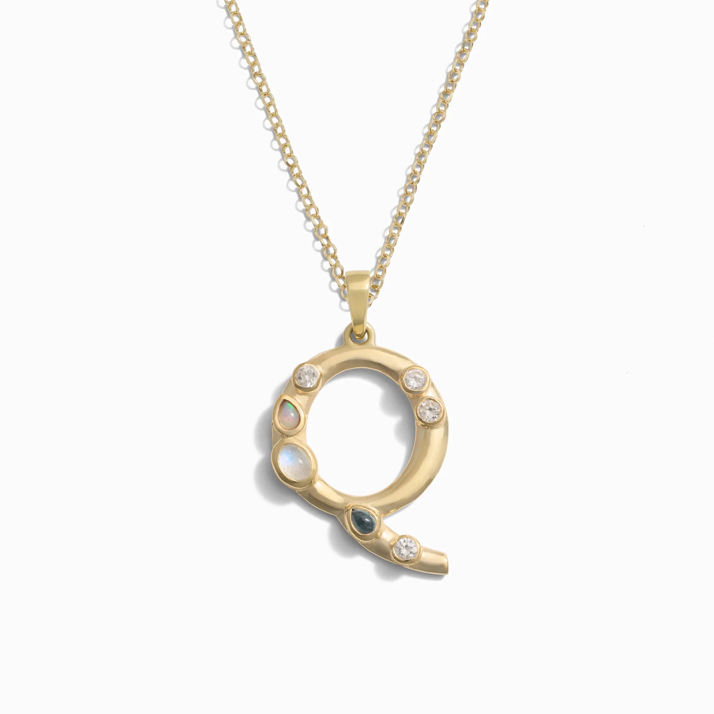 Awe Inspired's Gold Gemstone Initial Necklace features a pendant shaped like the letter "Q," adorned with small, bezel set gemstones.