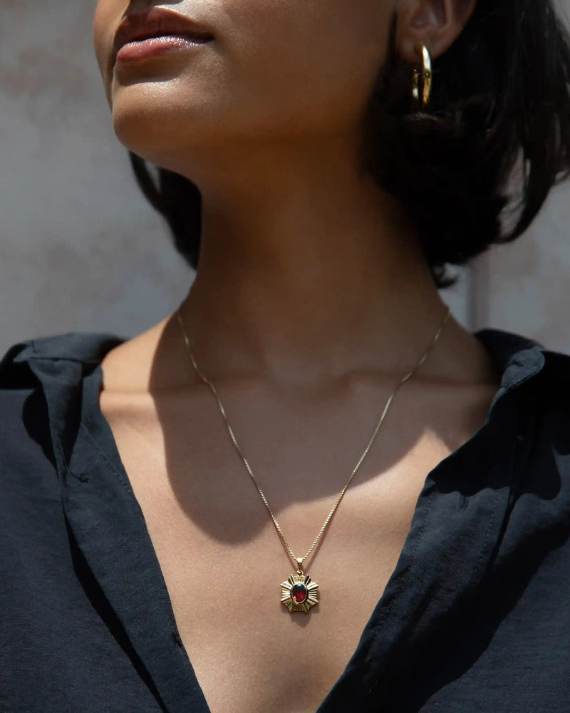 A person wearing the Awe Inspired Aura Pendant, with its gold necklace and striking red stone, enhancing their presence, paired with a sleek black button-up shirt.