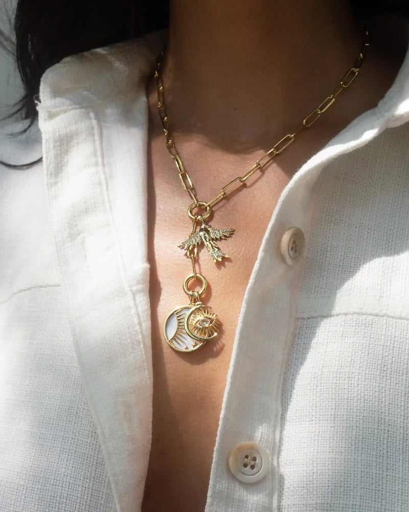 A person wearing a white collared shirt and the Awe Inspired Lariat Charm Collector Necklace, adorned with pendants such as a bird and a circular charm, each telling an awe-inspiring, unique story.