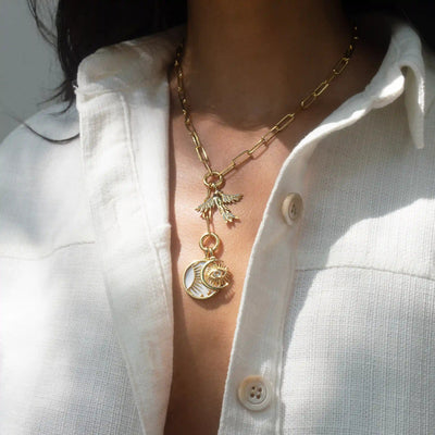 A person wearing a white collared shirt and the Awe Inspired Lariat Charm Collector Necklace, adorned with pendants such as a bird and a circular charm, each telling an awe-inspiring, unique story.