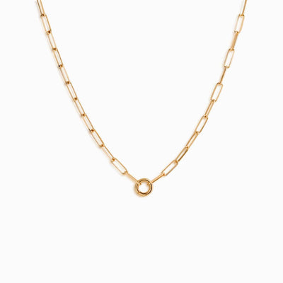 The Awe Inspired Convertible Charm Collector Necklace features a gold paperclip chain design with a circular clasp at the center, adorned with delicate amulets.