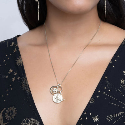 A person wearing a dark blouse with star and moon patterns, accessorized with the Awe Inspired Dancing in the Moonlight Charm Necklace, featuring multiple celestial-themed pendants, including a stunning Hecate Pendant.