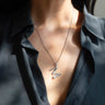 A person wearing a black shirt showcases the Awe Inspired Silver Gemstone Initial Necklace, featuring a statement size zigzag pendant adorned with bezel set gemstones.