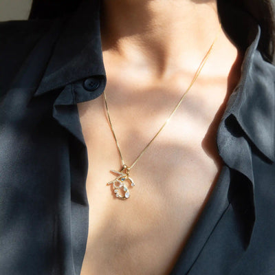 A person wearing a dark, partially open shirt and the Awe Inspired Gold Gemstone Initial Necklace, which boasts statement size initial charms alongside a pendant featuring starfish and shell designs.