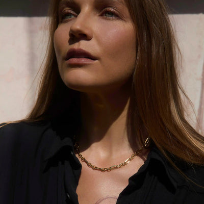 A woman with long brown hair, wearing a black top and the Awe Inspired Statement Chain Necklace, gazing upward.