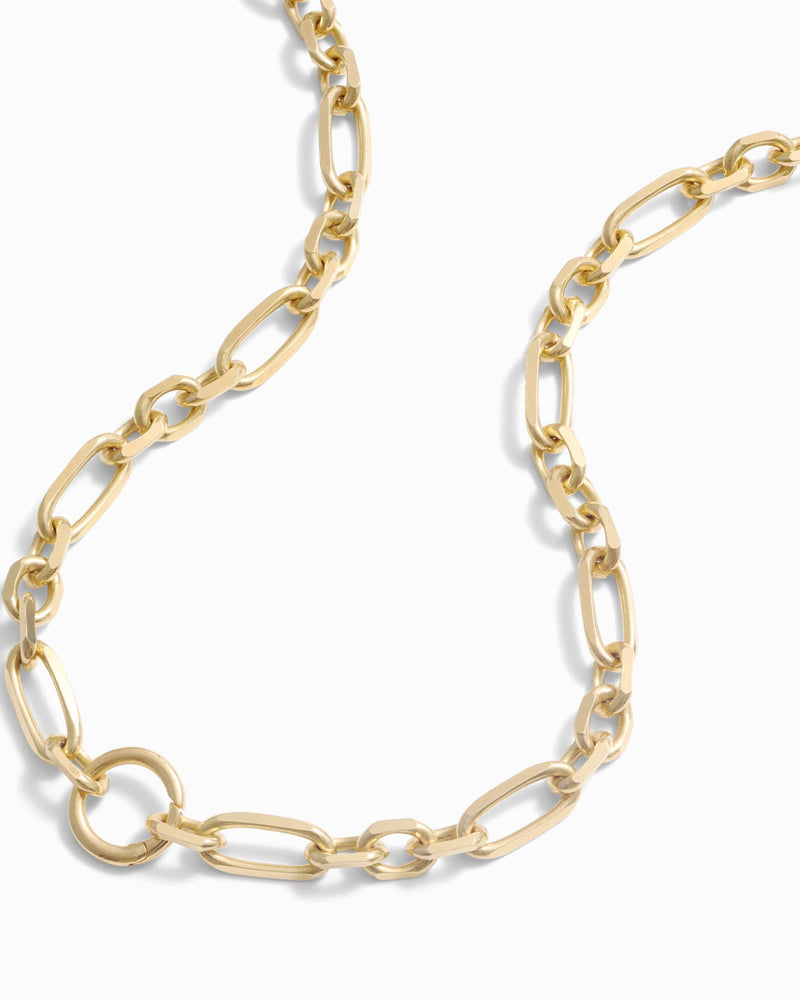 A close-up of a wide luxe link chain necklace with oval links and a small circular pendant. The Statement Single Charm Collector Necklace by Awe Inspired is elegantly laid out in a curved pattern against a plain white background.