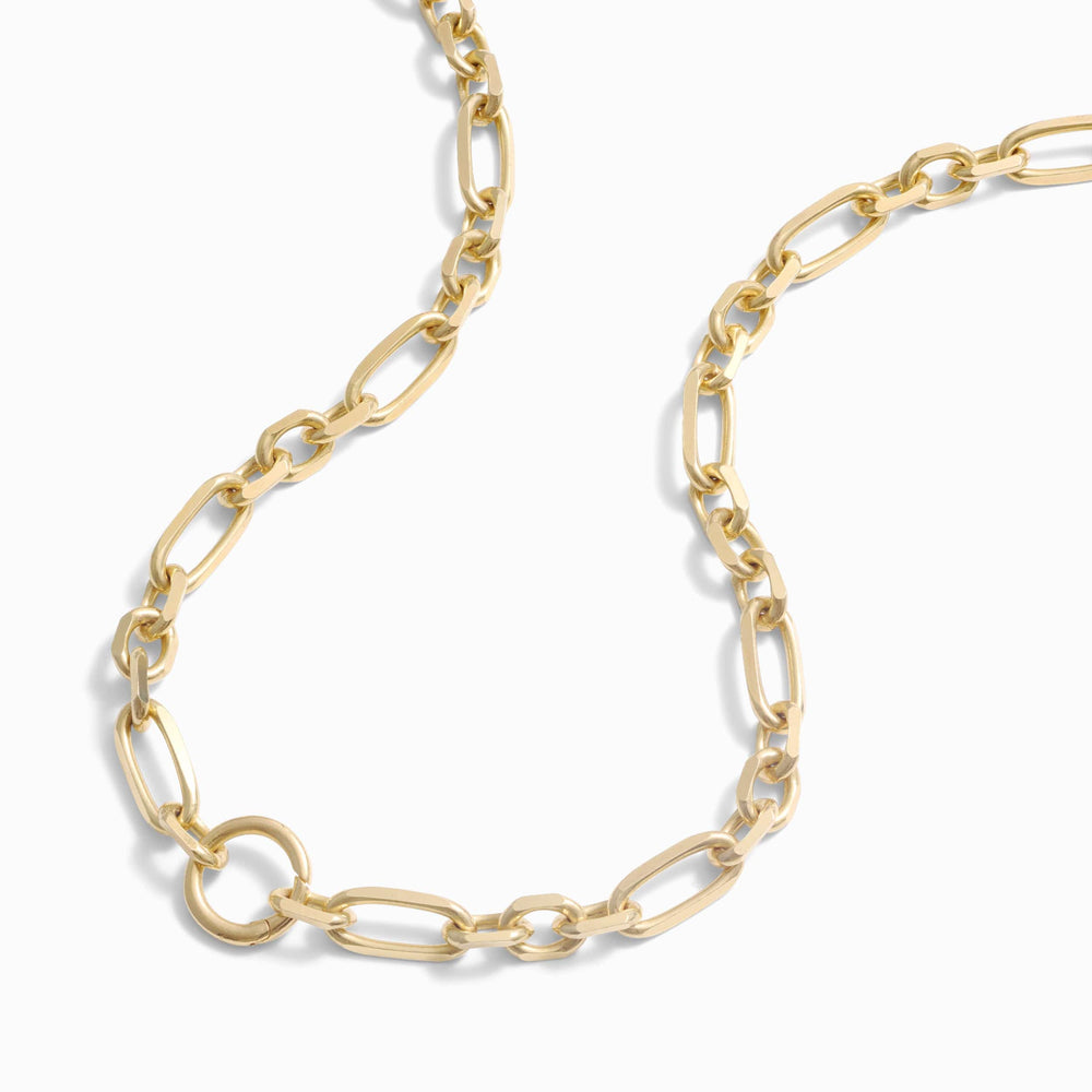A close-up of a wide luxe link chain necklace with oval links and a small circular pendant. The Statement Single Charm Collector Necklace by Awe Inspired is elegantly laid out in a curved pattern against a plain white background.