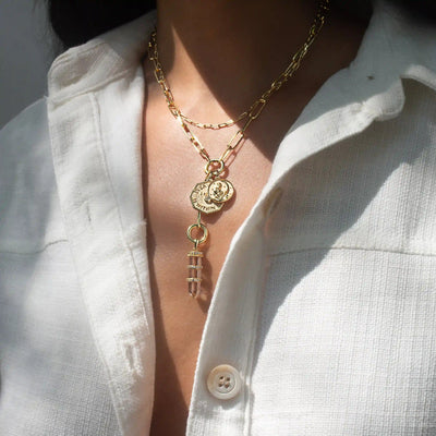 Close-up of a person wearing a white shirt and the Awe Inspired Manifestation Charm Lariat necklace, featuring layered gold pendants, including a coin inscribed "Everything I Need Is Within Me" and a sparkling crystal.