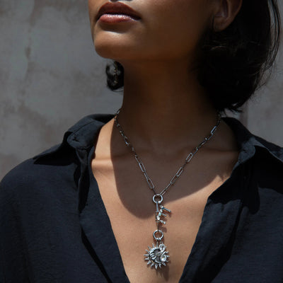 A person wearing a dark shirt and the Awe Inspired Silver Gemstone Initial Necklace, adorned with sun and key pendants as well as initial charms.