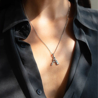 A person wearing a black button-up shirt with a Silver Gemstone Initial Necklace from Awe Inspired, featuring a pendant shaped like the letter "A".