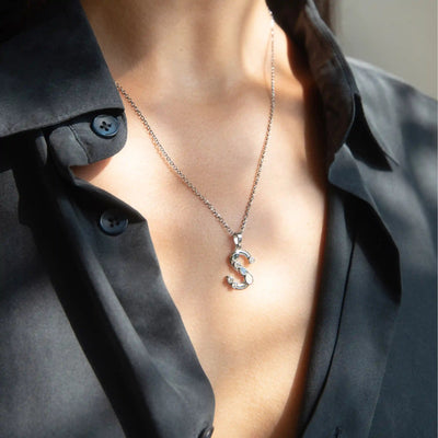 Person wearing the Awe Inspired Silver Gemstone Initial Necklace with a statement-sized "S" pendant over a black shirt, accented with bezel-set gemstones.